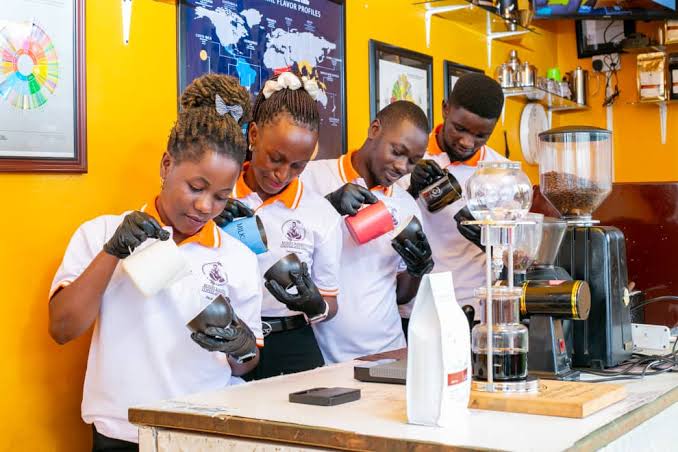 Bonny Barista trainees pouring latte art behind the coffee bar in Kampala